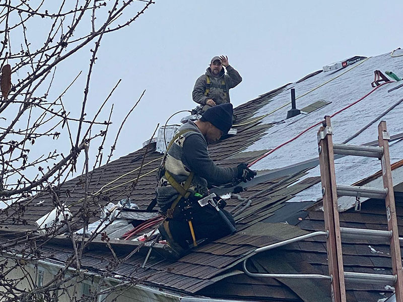 Close up of two High Definition Roofing workers installed new shingles on a residential roof, one of them is waving at the camera